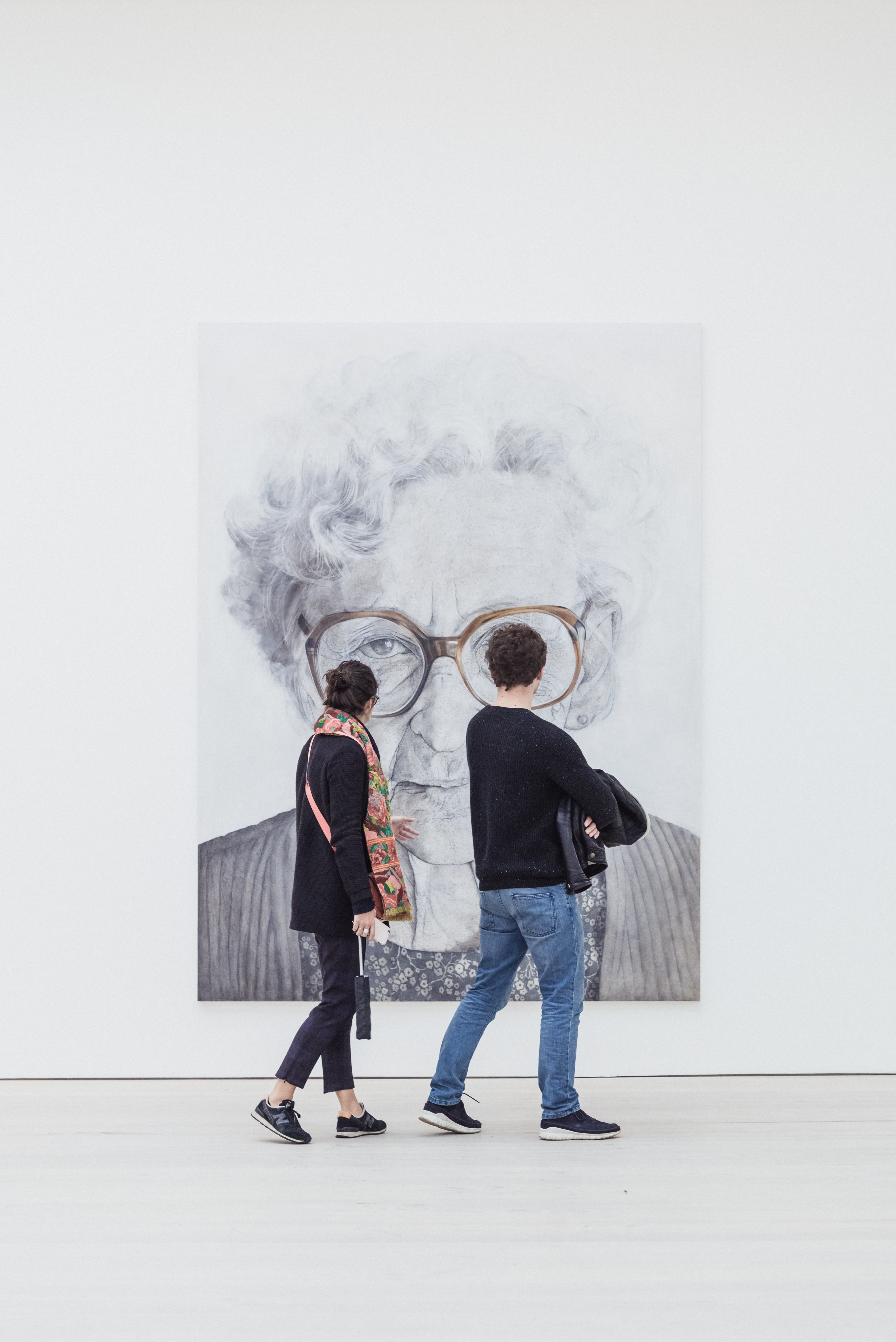 Portrait of an old lady looking at the camera with to people looking at the portrait.