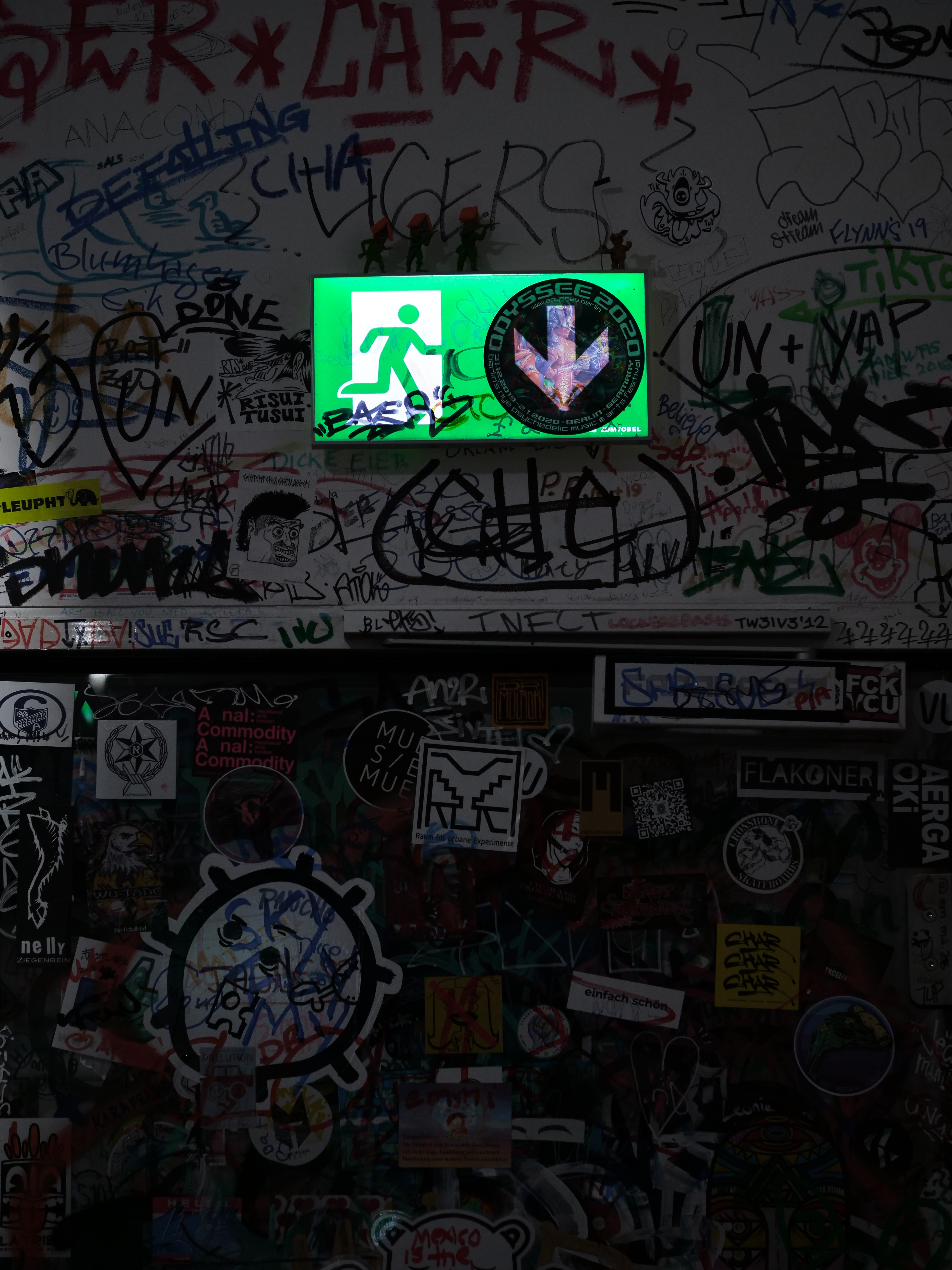 Green exit sign with grafitti on sign and surrounding walls.