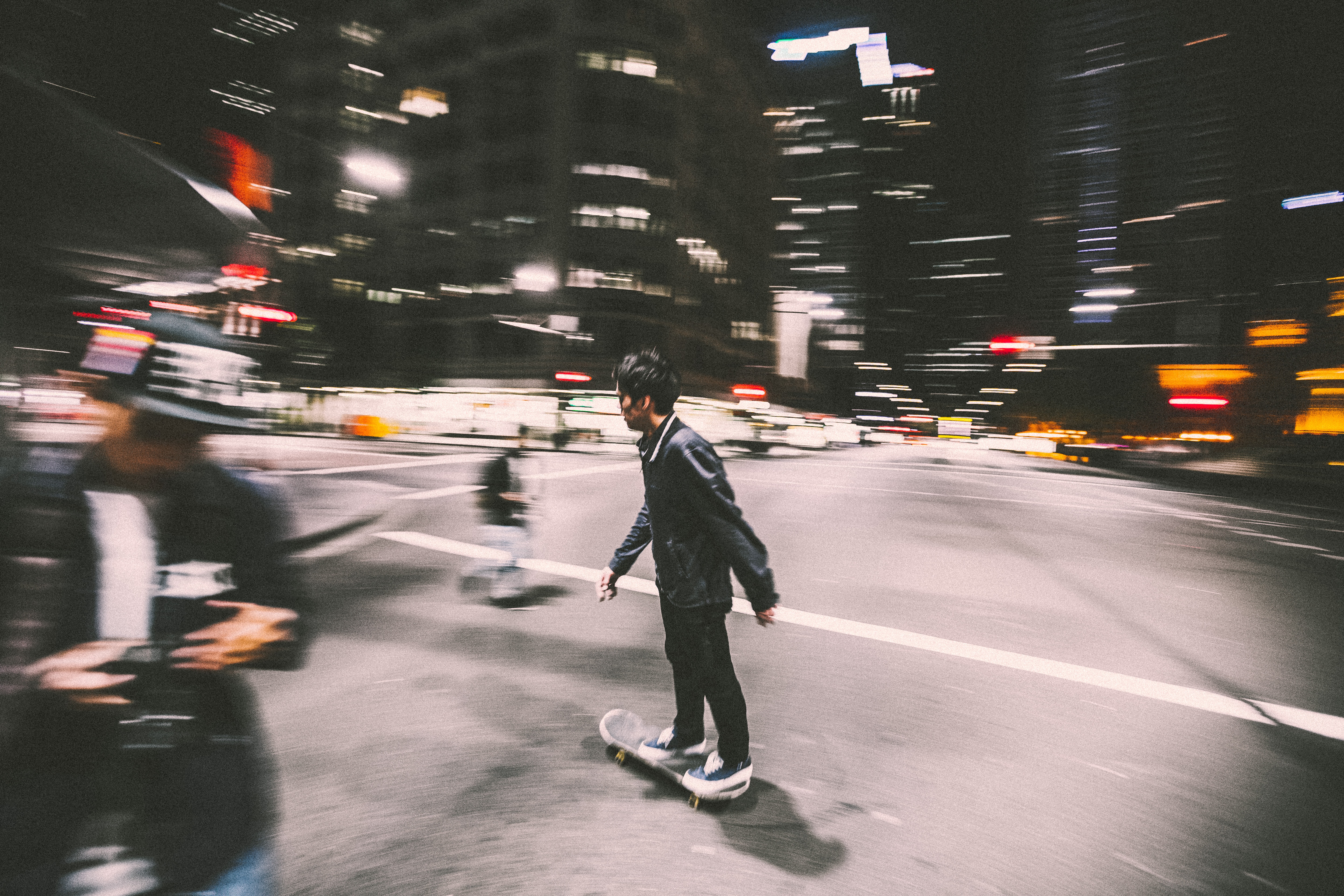 Man in black skates in a busy street with a blurry background.