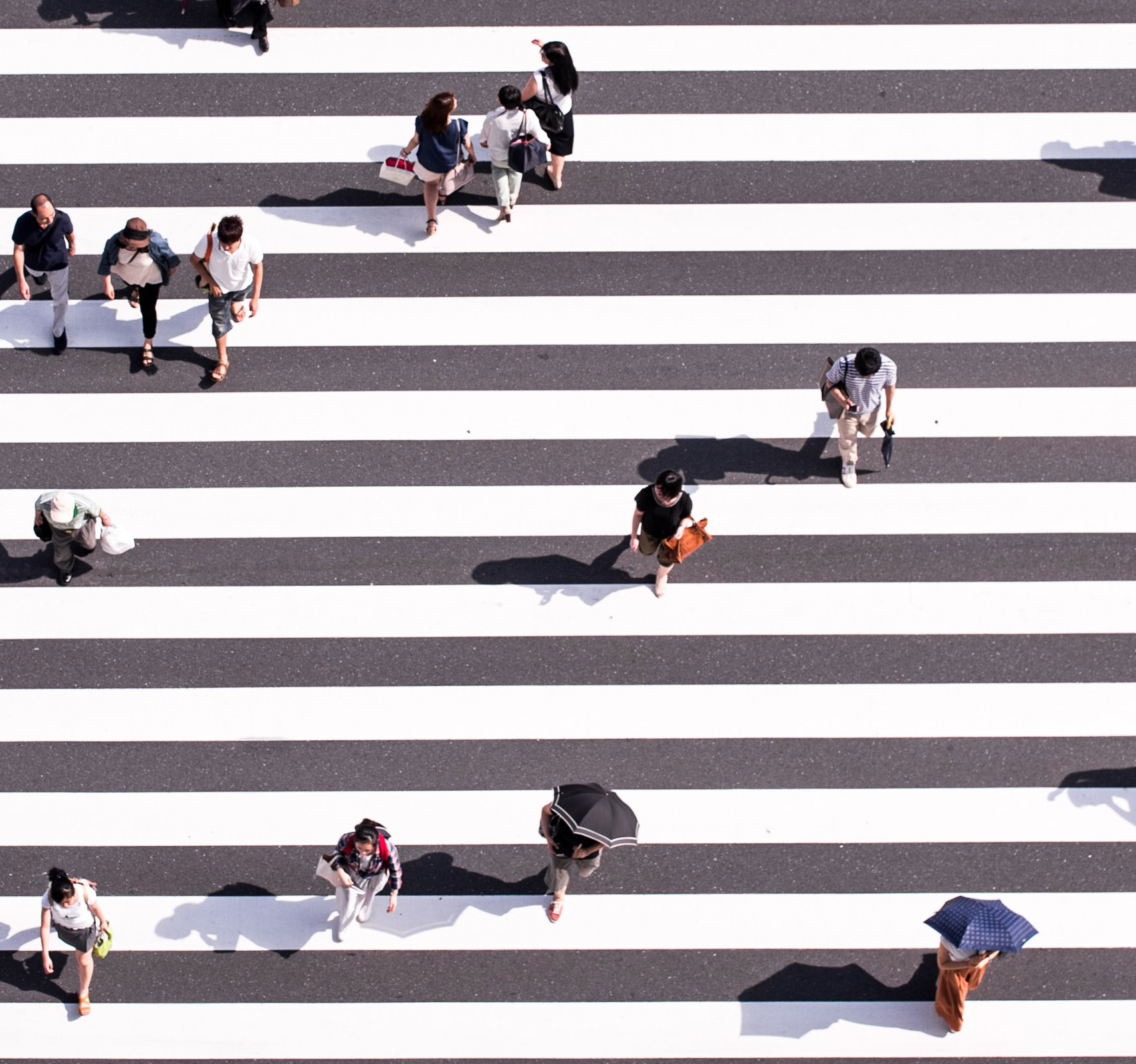 Ariel view of people crossing the street on a lined crosswalk.