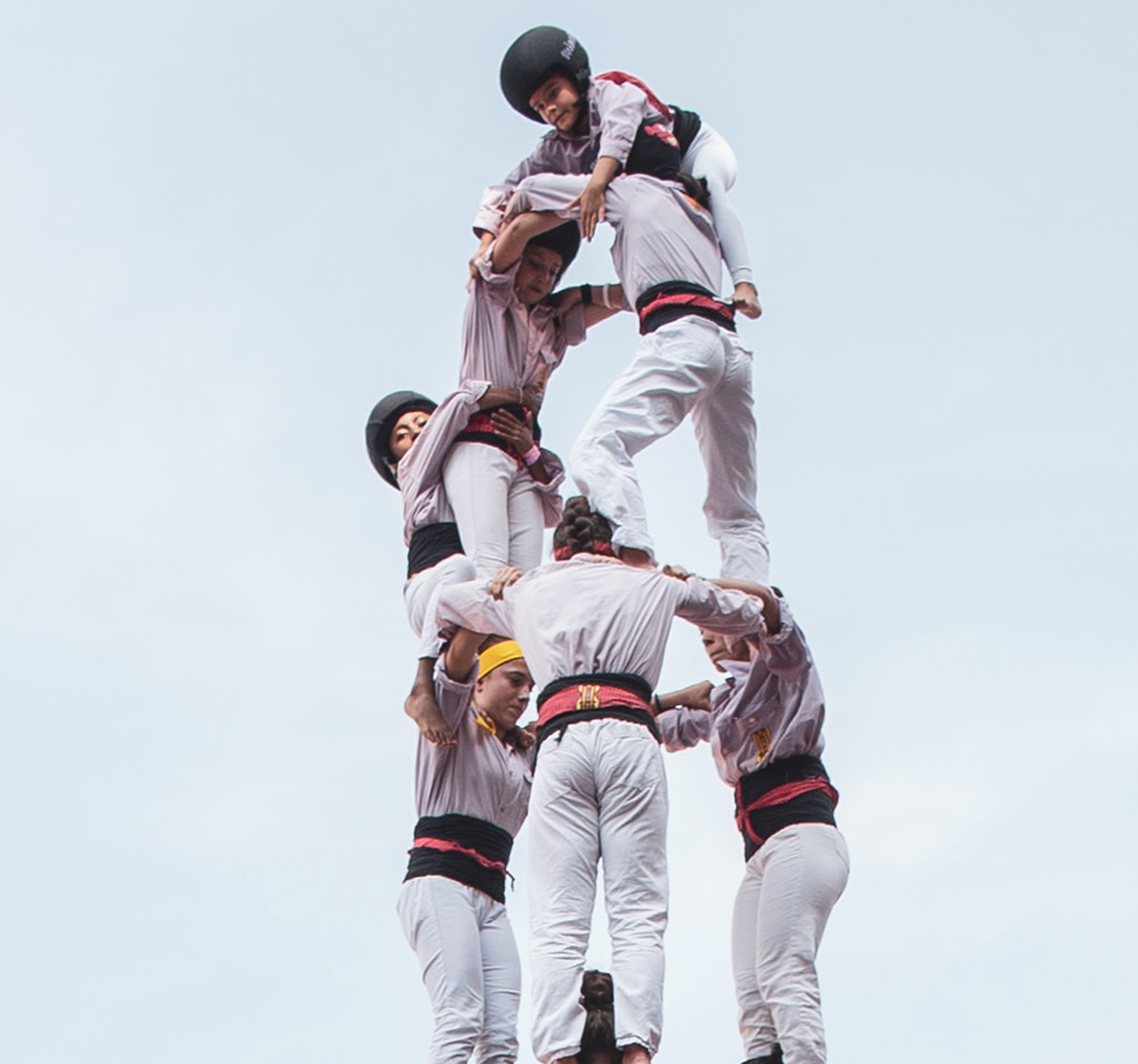 Men are stacked tall holding eachother up in all white outfits.