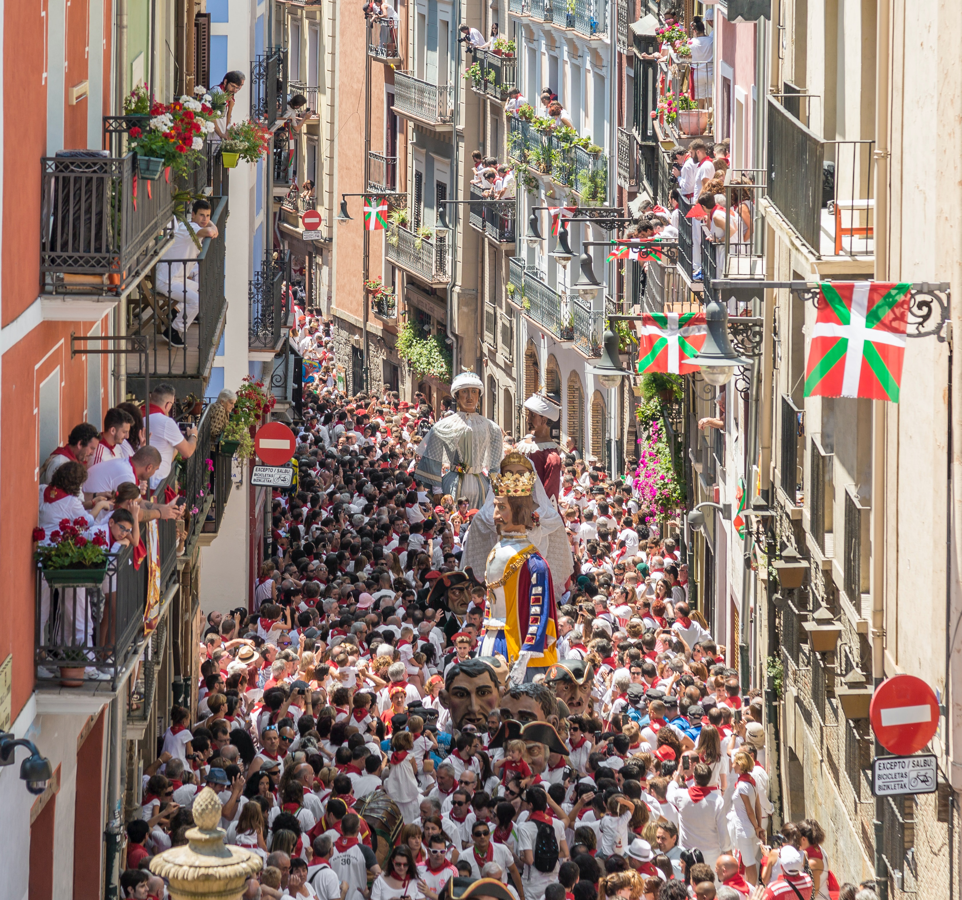 Very busy street where there is a parade with people carrying large statues of religious figures.
