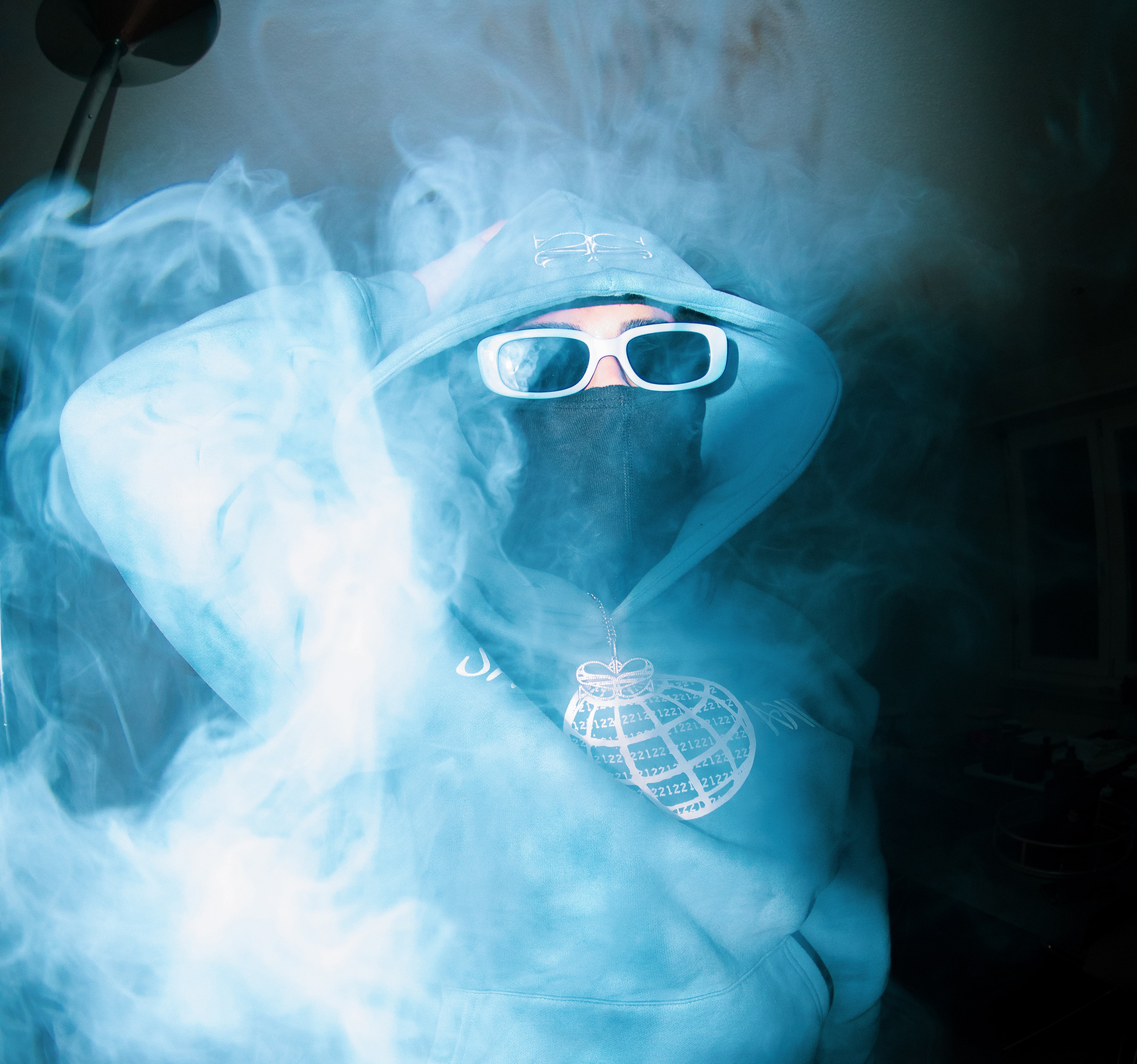 Man with a hood, sunglasses, and mask is surrounded by smoke.